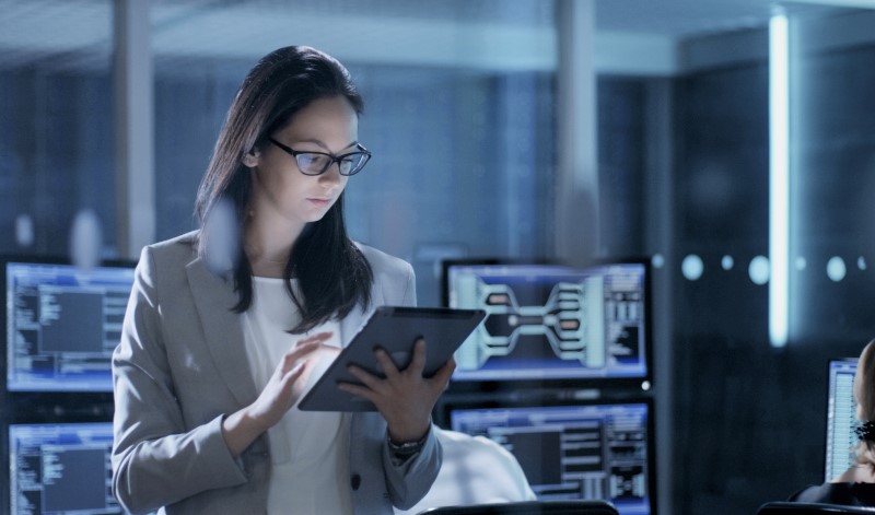 girl looking at tablet with computer screens in background - cybersecurity