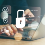 Securing data backups against ransomware. The image depicts a cybersecurity theme with a focus on data protection. In the foreground, hands are typing on a laptop keyboard, symbolizing user interaction with technology. Floating above the laptop is a large, glowing white padlock icon, representing secure access or cybersecurity. To the left of the padlock are three smaller icons: a cloud with arrows (representing cloud storage or data transfer), a shield with a checkmark (indicating security or protection), and a globe with an envelope (symbolizing global communication or email security). On the right side of the padlock is a semi-transparent login interface displaying "CYBER SECURITY" with placeholders for a username and password, emphasizing secure user authentication. The background is softly blurred, focusing attention on the icons and laptop interaction. The overall tone conveys the importance of cybersecurity in a connected digital environment.