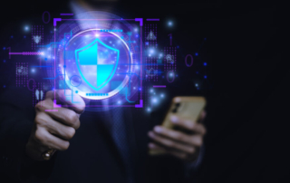 Threat sharing ransomware collaboration. A person in a dark suit is holding a smartphone while pointing forward. A glowing blue digital shield with a cyber-themed holographic security interface is projected in front of them. The background is dark with binary numbers (0s and 1s), circuitry, and floating icons, giving it a high-tech cybersecurity feel.