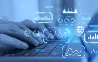 Compliance-Driven Patch Updates. Close-up of a person's hands typing on a laptop keyboard. Bright blue futuristic graphics — including graphs, pie charts, world maps, and percentages — float around the hands, suggesting data analytics, financial modeling, or business intelligence work happening in real time.