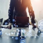Encrypted Backup Services. Several people in business attire stand around a conference table with laptops open. The scene is overlaid with floating digital icons — like magnifying glasses, graphs, Wi-Fi symbols, cloud storage, and security shields — suggesting a high-level meeting about technology, cybersecurity, or digital strategy. Warm light filters through the background.