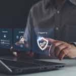 Patch management for ransomware defense. This image shows someone interacting with a holographic interface emerging from a laptop. They touch virtual screens displaying icons indicating password entry, multi-factor authentication (MFA), and a shield icon confirming successful login. The person is in professional attire, reinforcing the concept of secure digital identity verification and cybersecurity.