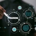 Real-Time Network Monitoring. A close-up of a hand holding a stylus or pen, pointing at a futuristic digital interface. The word "TRAINING" is highlighted in the center of interconnected icons: a target, a gear, a lightbulb, an open book, and groups of people. The visual suggests concepts of learning, skill development, and structured knowledge building in a digital or corporate environment.