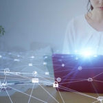Patch Deployment Automation. A woman sits at a desk using a tablet, partially obscured by a bright digital overlay of interconnected icons such as locks, clouds, and gears. The imagery represents digital security and network communication.