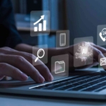 Phishing Simulation Training for Teams. Hands typing on a laptop keyboard. Floating icons above the laptop represent email, file search, AI processing, cloud storage, and phone support. It symbolizes multitasking in a digital workspace and interaction with advanced software systems.