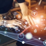 Ransomware incident reporting system. Hands type on a laptop in a warmly lit environment while a burst of glowing digital icons—representing Wi-Fi, search, security, and mobile apps—float above the keyboard, evoking the idea of digital transformation and connectivity.