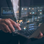 Secure Backup for Business Continuity. A close-up of a person’s hands using a laptop, overlaid with digital data dashboards and global analytics visuals, suggesting business intelligence or data analysis.