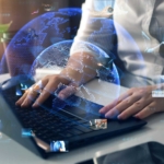 IT team ransomware training. A person in a white shirt works on a laptop, surrounded by holographic globes and floating images of people and graphs.