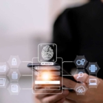 SD-WAN Security Optimization. A person holding a smartphone, with a transparent holographic interface showing a fingerprint icon, padlock, and other security-related symbols hovering in front of the device.