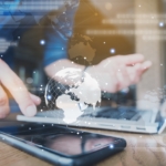 Decentralized backups ransomware benefits. A businessperson uses a smartphone while working on a laptop. A glowing map of the globe and a stream of binary code overlay the image, signifying global communication, data transfer, or international cybersecurity operations.