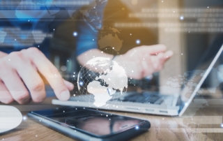 Decentralized backups ransomware benefits. A businessperson uses a smartphone while working on a laptop. A glowing map of the globe and a stream of binary code overlay the image, signifying global communication, data transfer, or international cybersecurity operations.