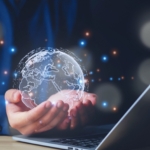 identity-threat-prevention Identity Threat Prevention. A person cupping a holographic globe of Earth over an open laptop. The scene is surrounded by glowing digital particles, evoking a sense of global connectivity, cloud technology, or digital transformation.