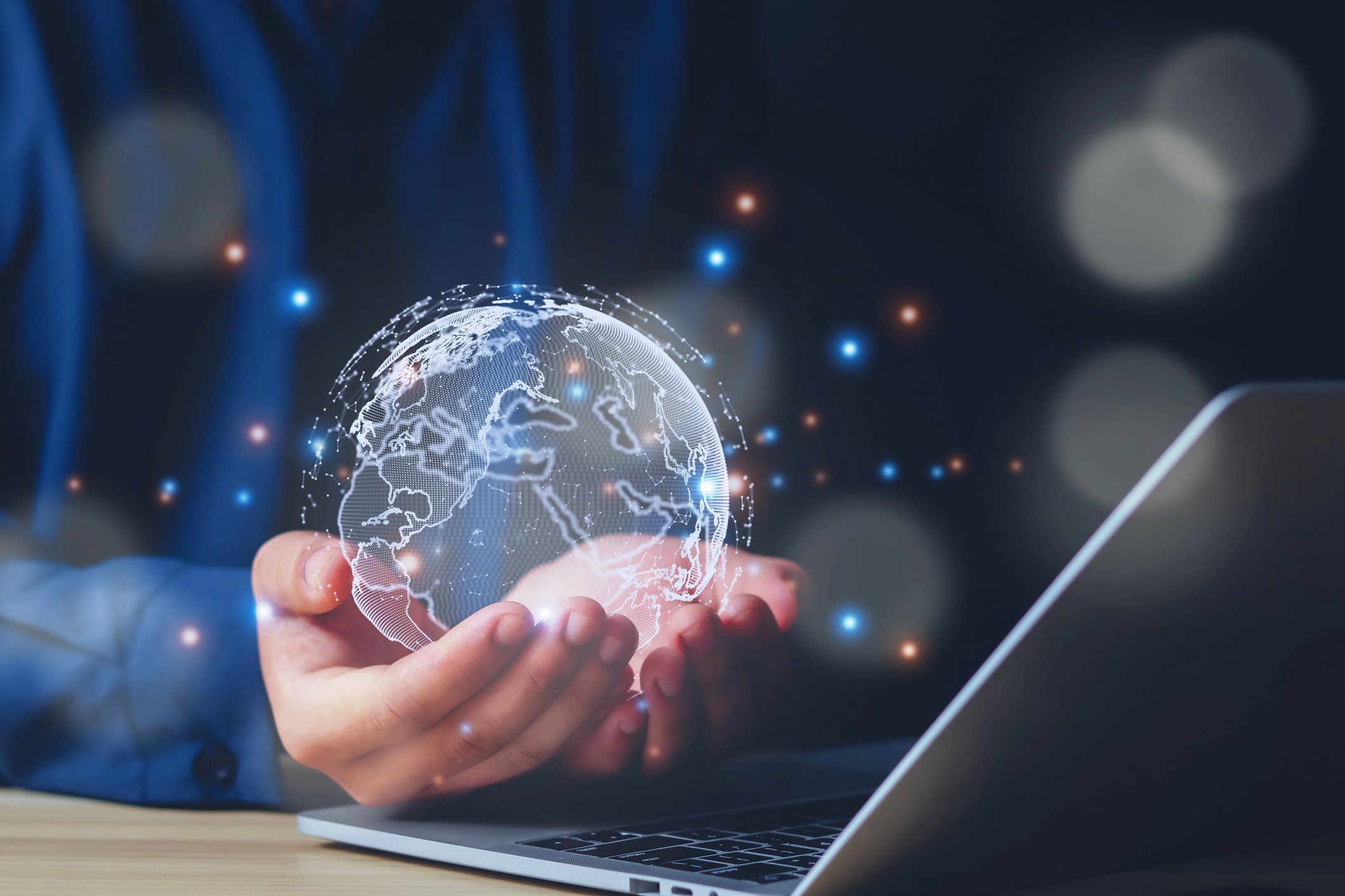 Identity Threat Prevention. A person cupping a holographic globe of Earth over an open laptop. The scene is surrounded by glowing digital particles, evoking a sense of global connectivity, cloud technology, or digital transformation.