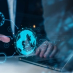 Ransomware-as-a-Service Insights. A person in a business suit points at a glowing holographic globe, with other transparent icons and lines radiating from it, positioned over a laptop keyboard.