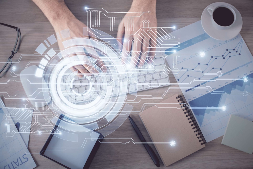 Ransomware recovery communication protocol. A top-down shot of someone typing on a white keyboard surrounded by notebooks, papers, a coffee cup, and eyeglasses. A translucent circular HUD (heads-up display) graphic overlays the scene, symbolizing data entry or secure documentation.
