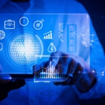 Threat Intelligence Automation. Hands holding a tablet device, with a glowing blue holographic interface showing icons for business, finance, and technology, all centered around a bright digital sphere.