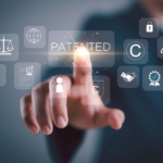 Immutable Architecture for Ransomware. A person pointing at a virtual screen displaying icons related to intellectual property—like a padlock, copyright symbol, checkmark, balance scale, and the word “PATENTED.” The background is dark with a business attire silhouette.